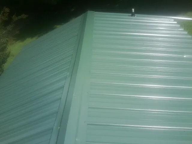 New green metal panels meeting at the ridge of a roof — Flat Roof Repair work by our crew in Amity