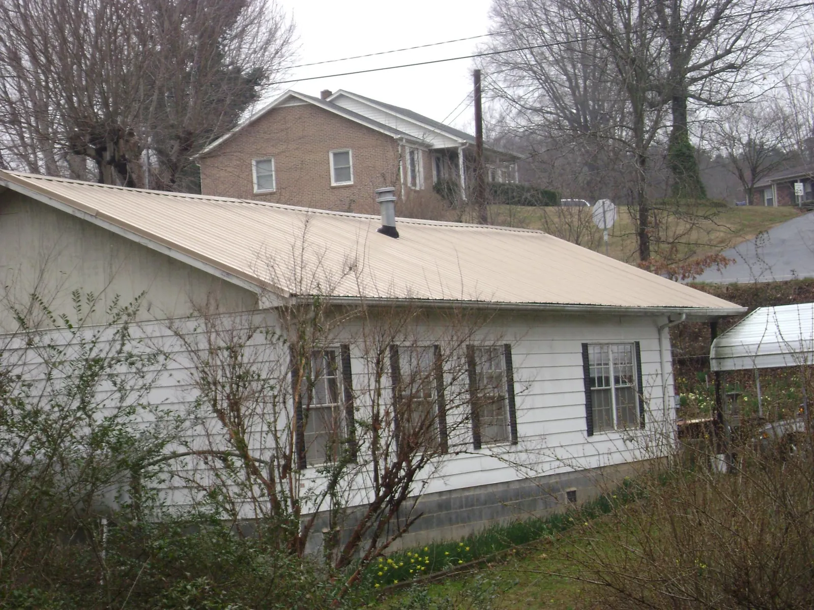 Tan metal roof on a white sided house set into a hillside — Commercial Roofing by Roofing Brothers in Amity