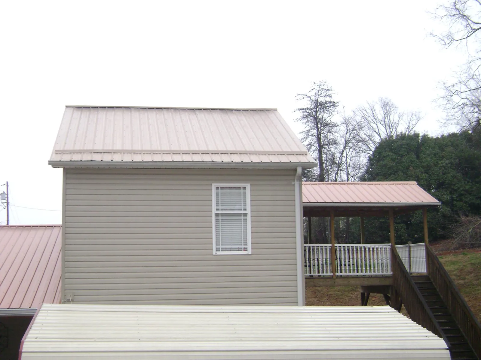 Tan metal roofs on a two story addition and attached porch, from a Roof Replacement job in Amity